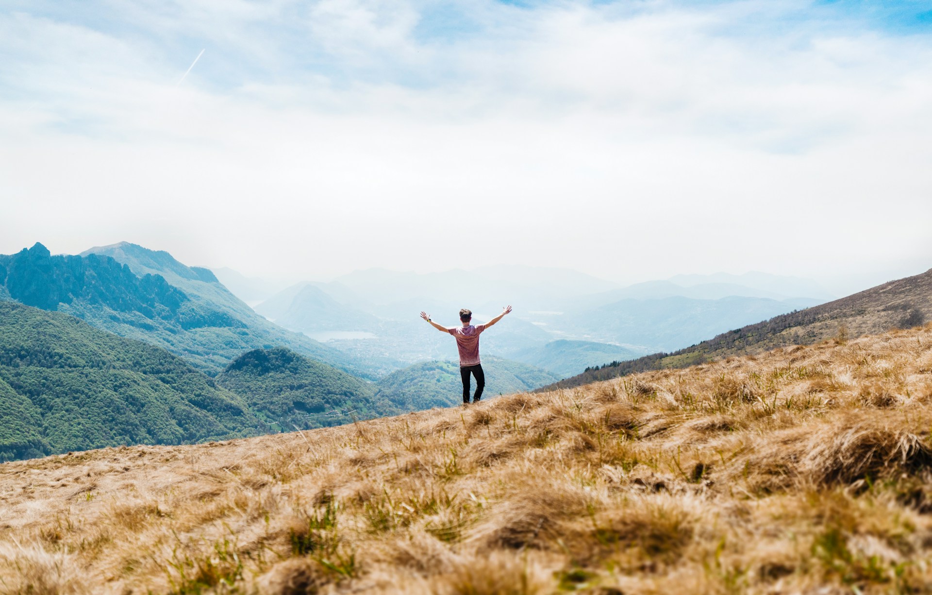 Person standing on a mountain ridge with arms raised, looking out over misty hills and open landscape. credits: dino reichmuth